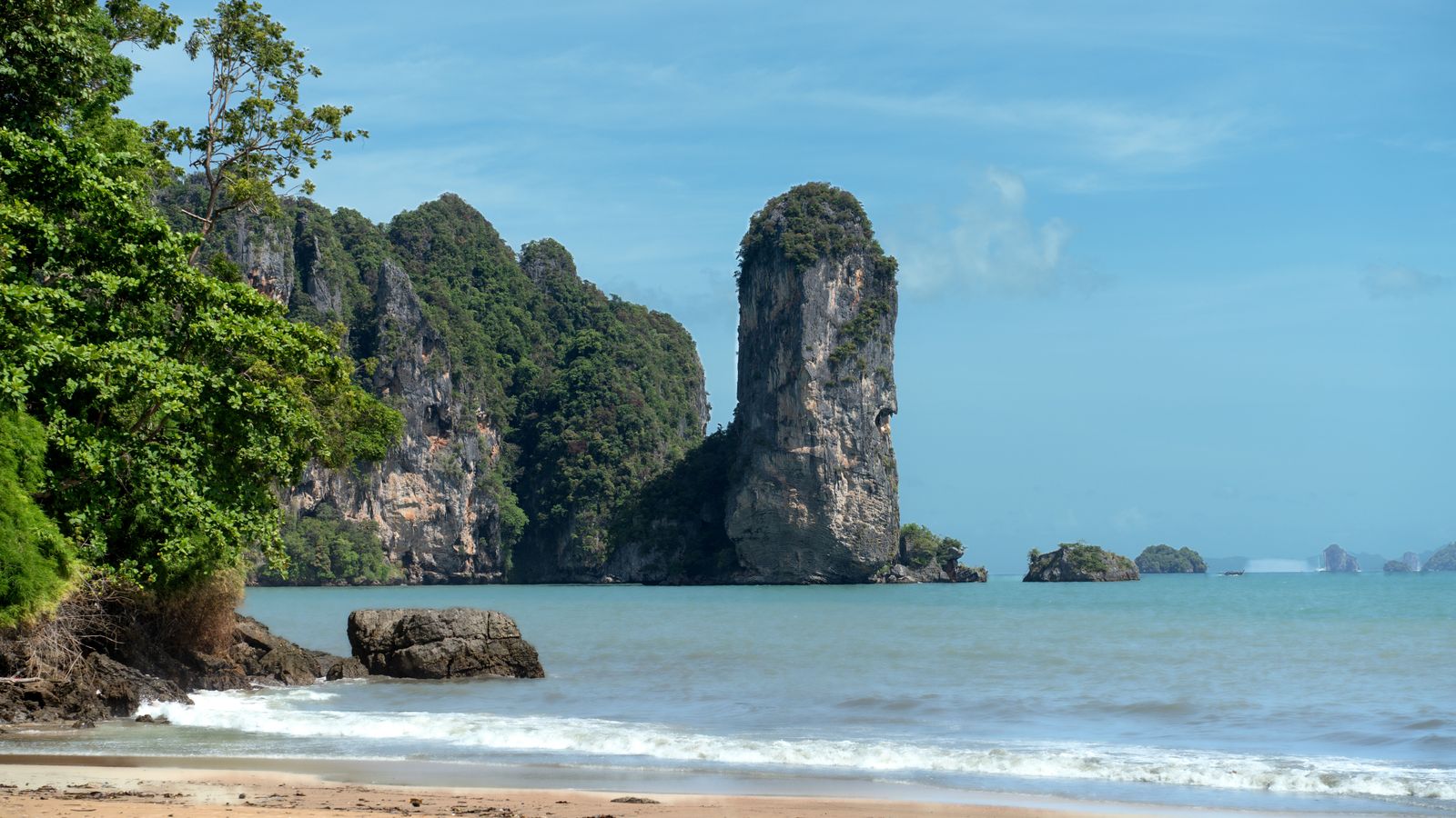 Limestone cliffs rise beyond the sandy shoreline and blue water at Ao Nang, Krabi.