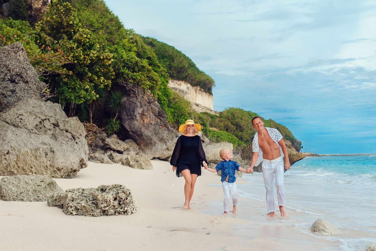 Two parents and their young son holding hands and walking together on a beach in Bali.