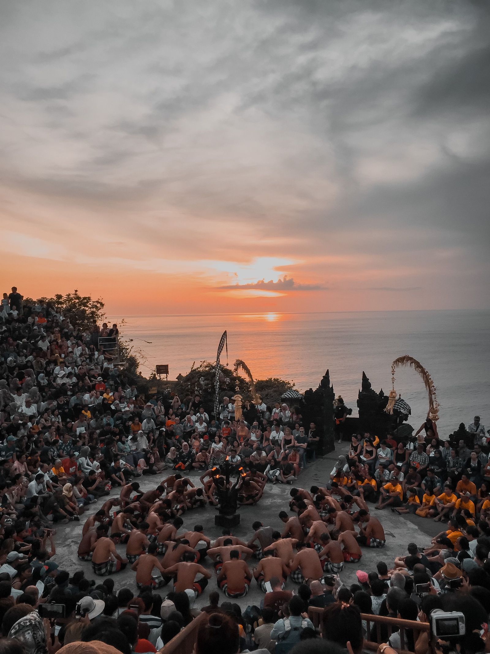 An audience watches a Kecak performance above the sea at Uluwatu as the sun sets.
