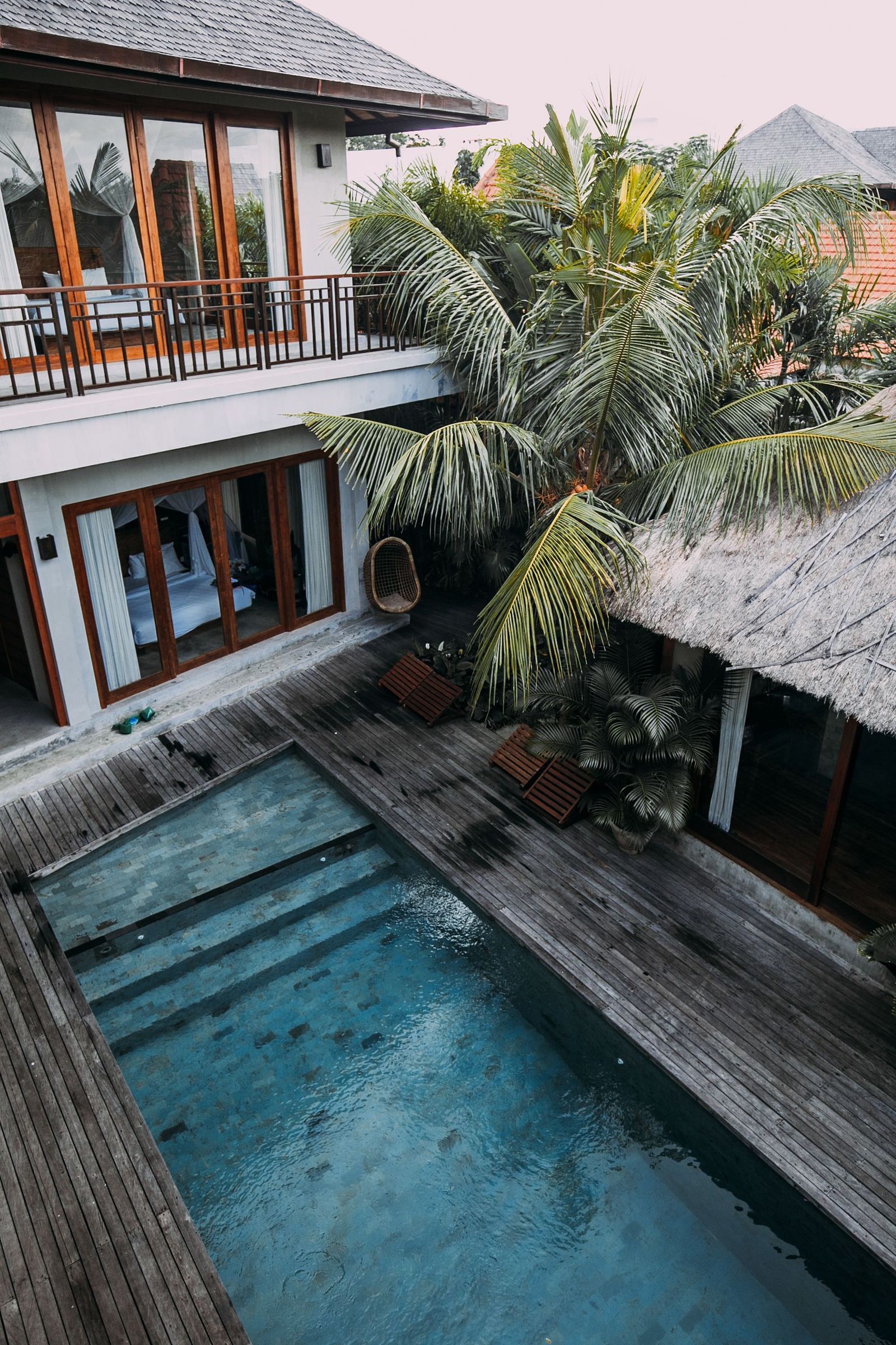 A villa balcony and a shaded pool surrounded by palms in Bali.