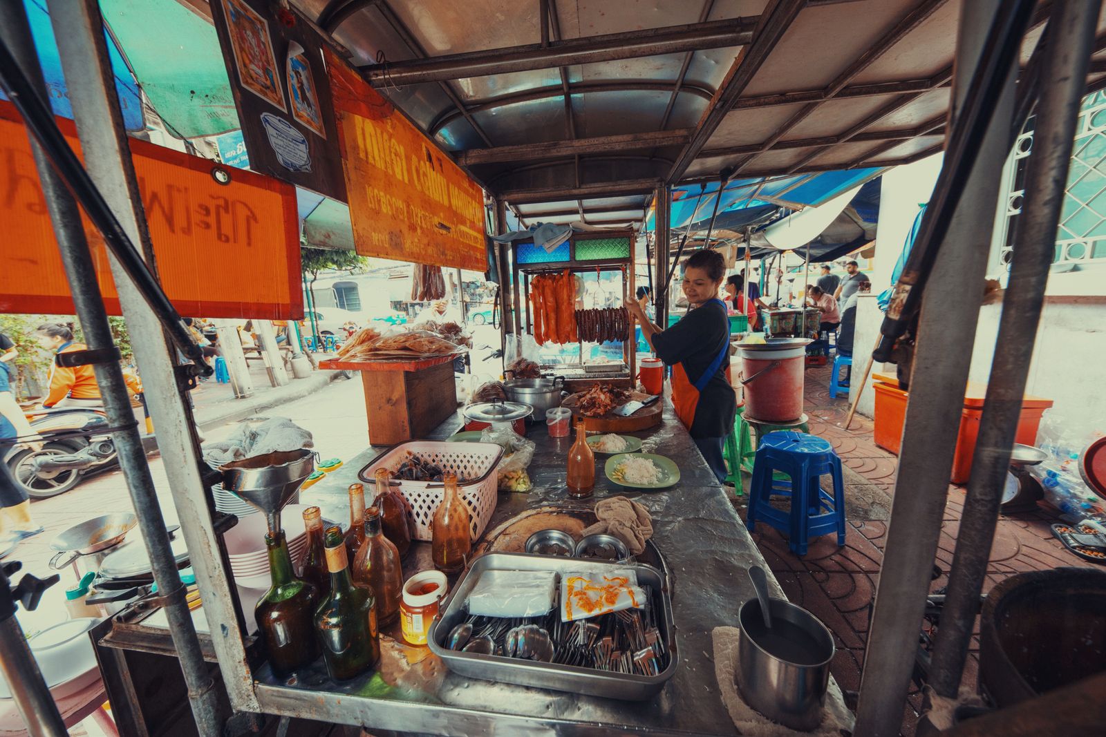 A vendor works behind a counter of pots and freshly prepared dishes at a Bangkok food stall.