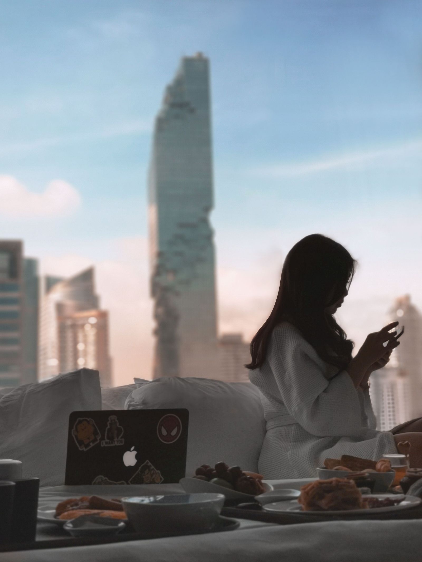 A guest sits by a hotel-room window overlooking Bangkok’s skyline in the morning.