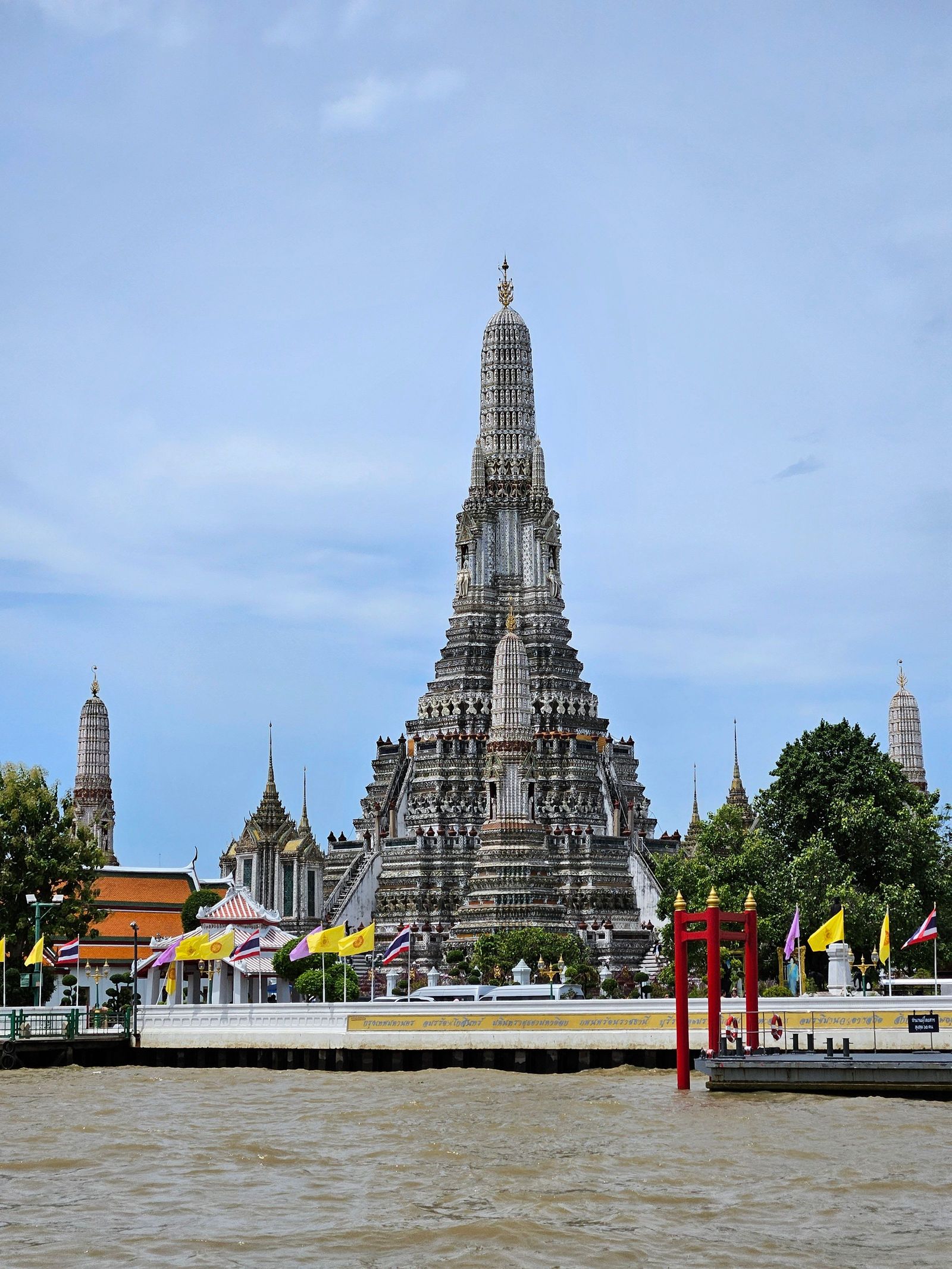Wat Arun’s central spire rises above riverside temple buildings beside the Chao Phraya River in Bangkok.