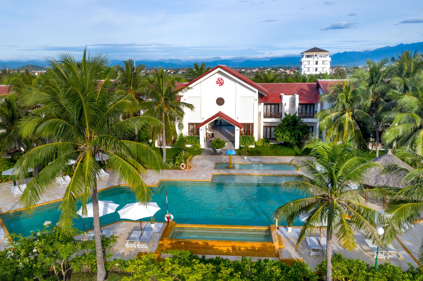 Palms surround a resort swimming pool and red-roofed buildings in Hoi An, Vietnam.