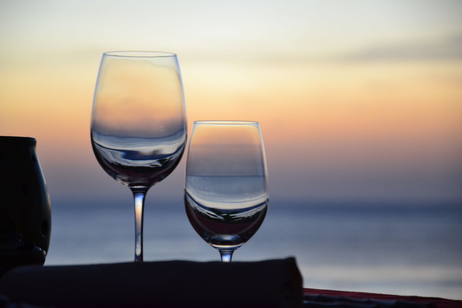 Two wine glasses on a dining table overlook Jimbaran Bay in the evening light.