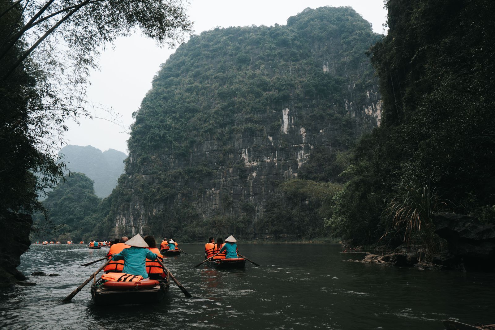 Visitors in small rowing boats travel between tall limestone cliffs in Ninh Binh.