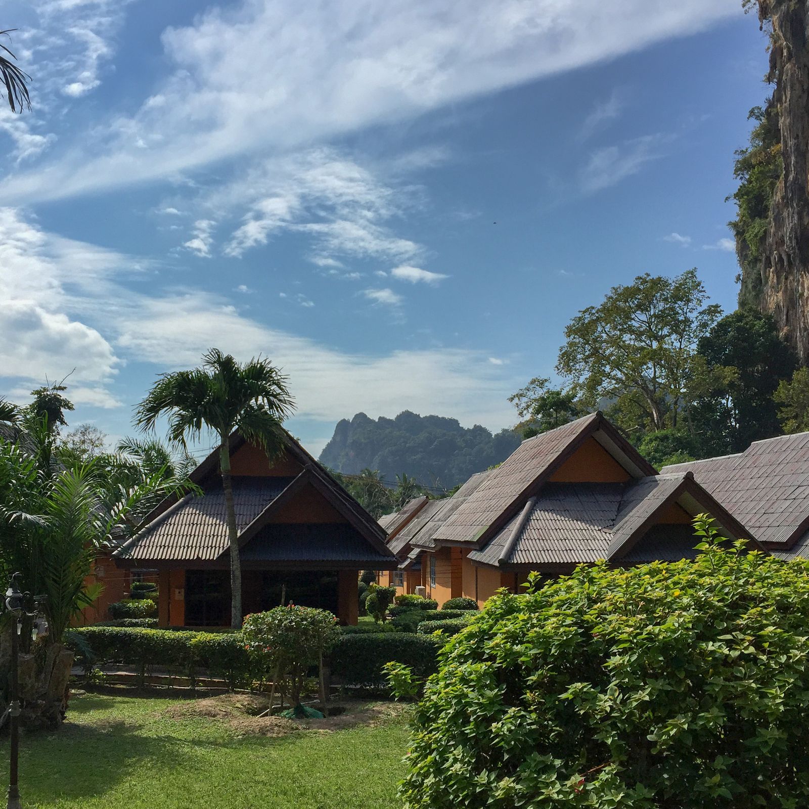 Timber resort bungalows and palms sit beneath limestone cliffs at Railay, Thailand.