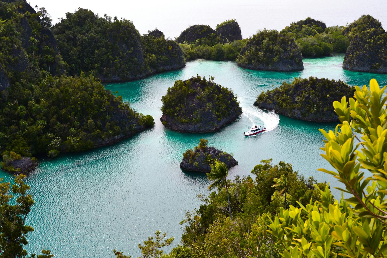 A small boat curves through turquoise water between forest-covered limestone islands in Raja Ampat.