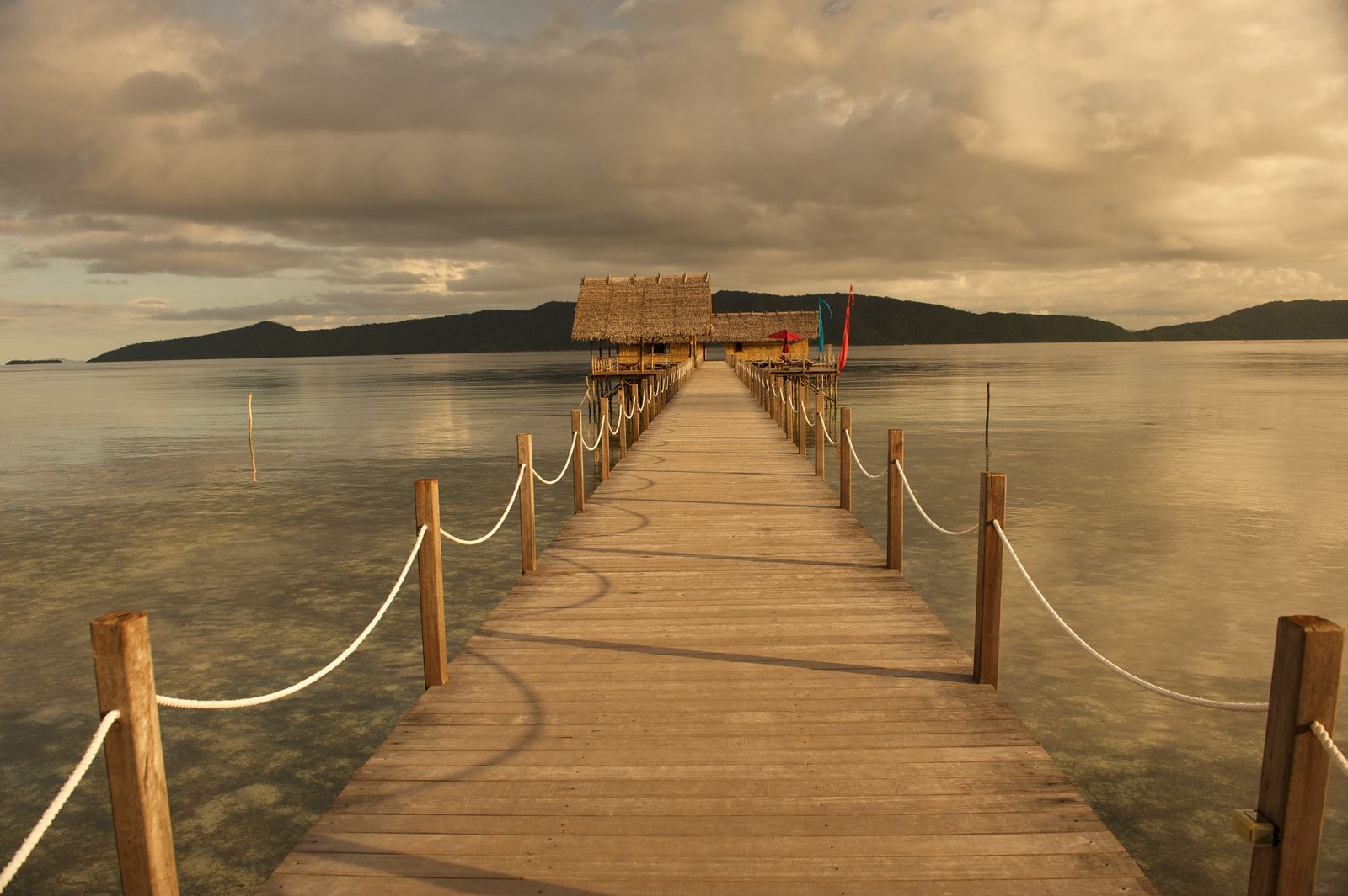 A wooden jetty leads to thatched buildings beside the water at Sawinggrai village in Raja Ampat.