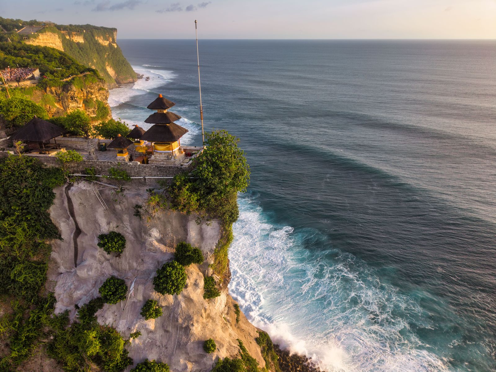 Uluwatu Temple stands on a limestone cliff above the ocean in warm evening light.